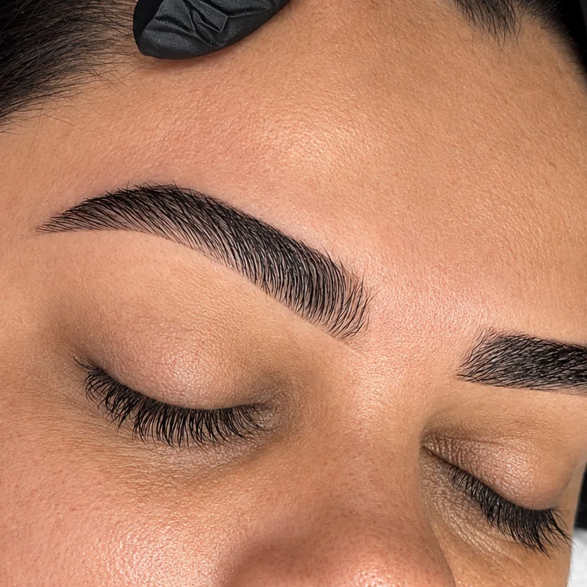 Detalhe do desenho de sobrancelhas durante atendimento, com olhos fechados.